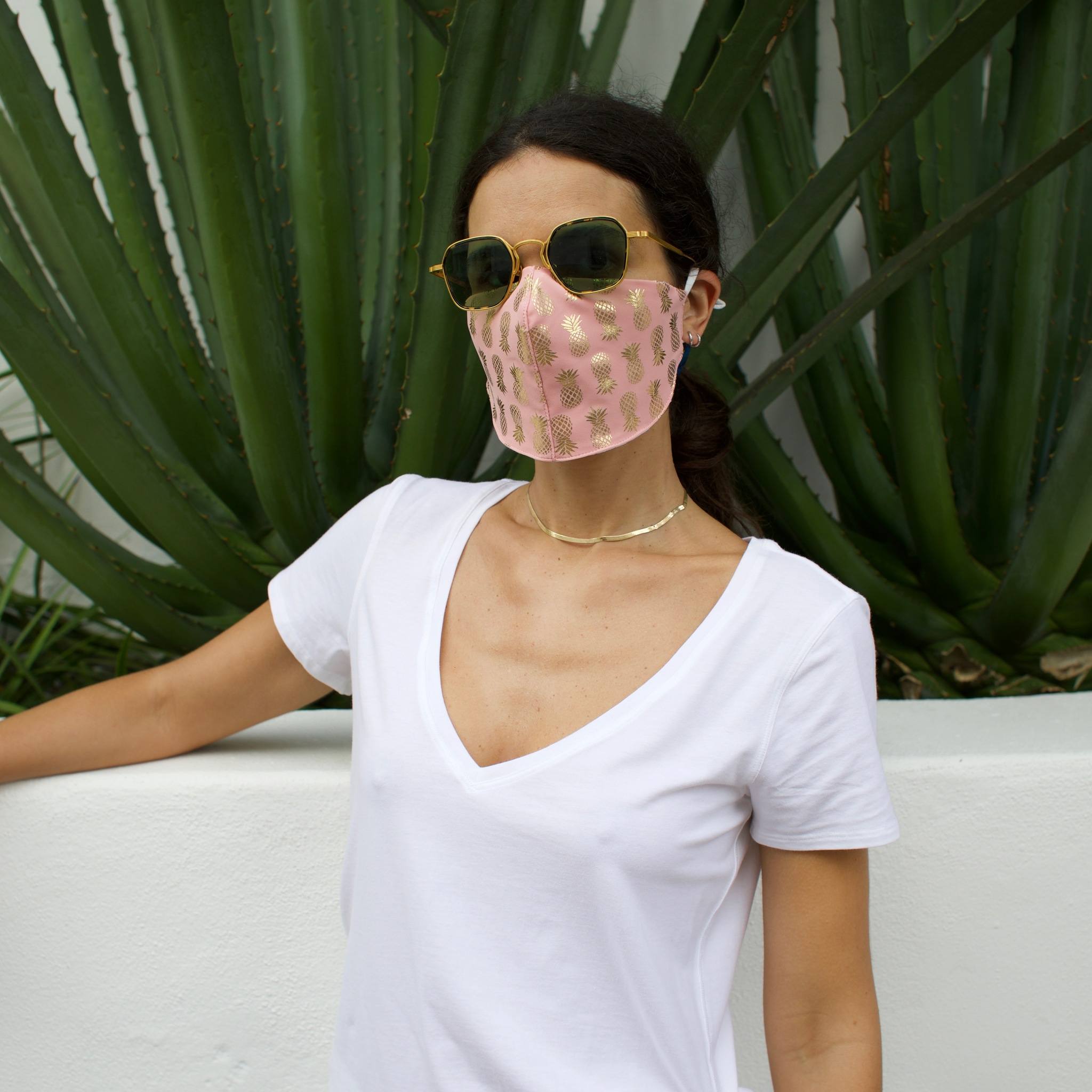 Woman in front of a cactus wearing a pink face mask with gold pineapples.